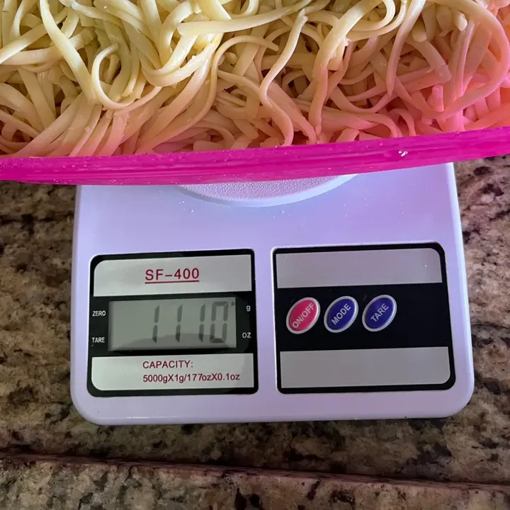 Pote de macarrão sobre uma balança SF-400 de plástico branca; o pote passa das bordas da plataforma redonda e o visor marca 1110 g.